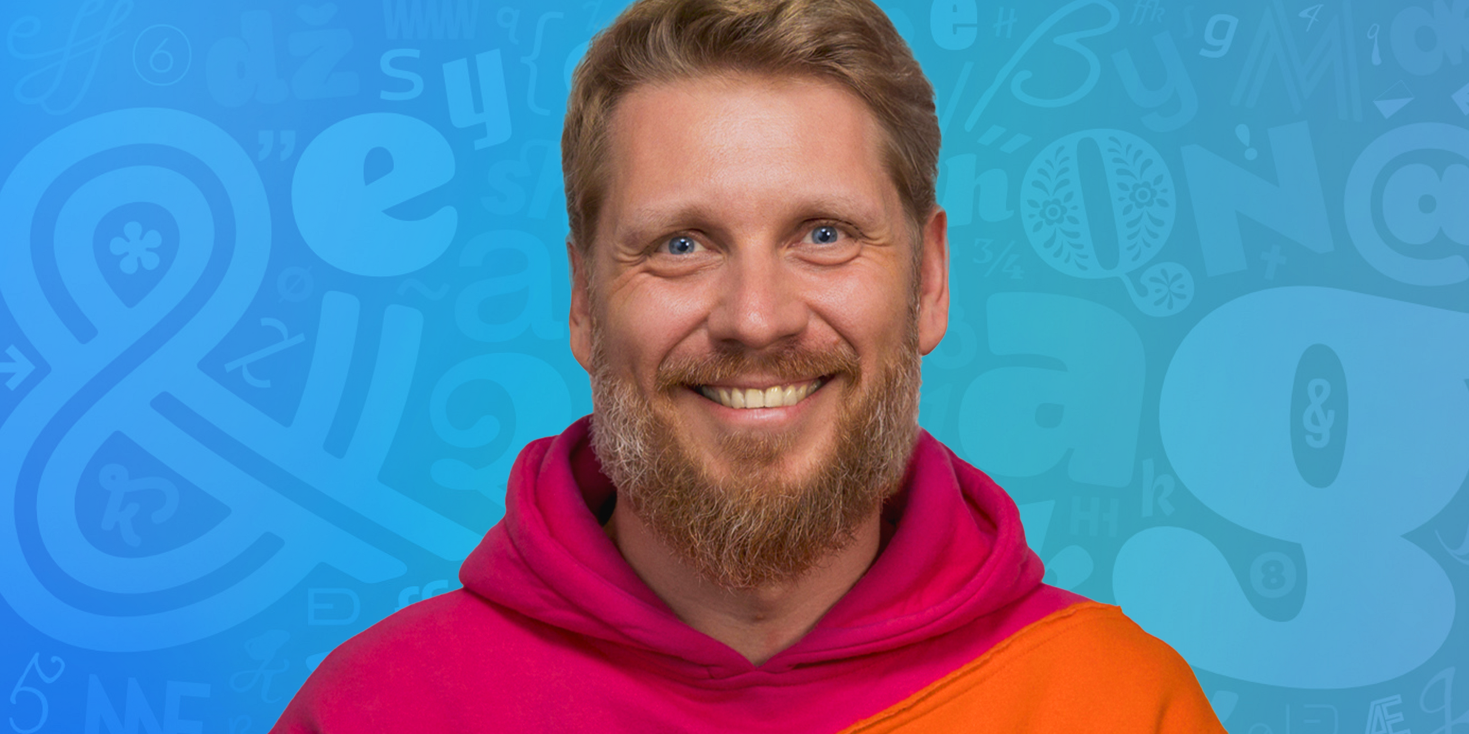Horizontal headshot of Roch Modrzejewski in a pink and orange hoodie, smiling in front of a blue background decorated with lighter blue glyphs (letters and symbols) in various sizes and positions.
