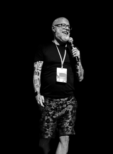 Black and white photo of Dan Rhatigan speaking on stage at Dia Tipo, microphone in hand.