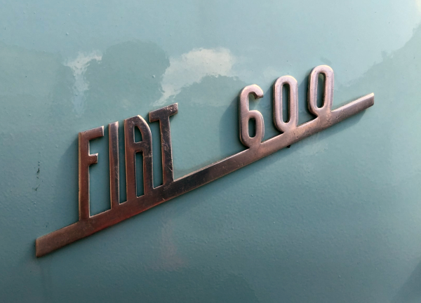 Photo of silver Fiat logo reading "FIAT 600" on light blue background. Photo by Giuseppe Salerno.