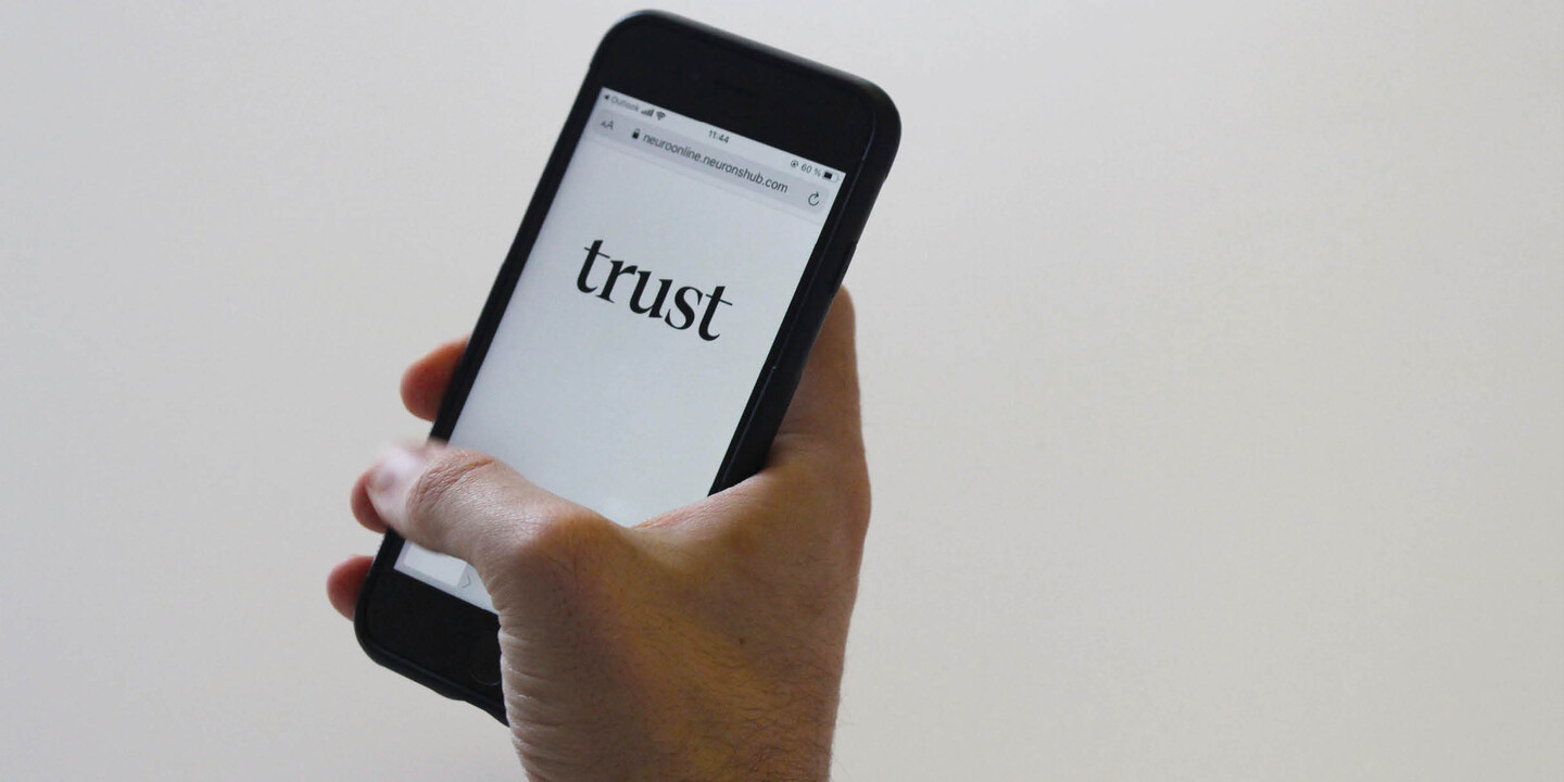 Hand holding iphone with a screen showing the word "trust" in Cotford Display typeface.