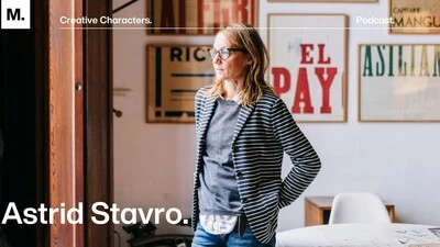 Astrid Stavro standing in a well lit room with framed typographic posters on the wall behind her.