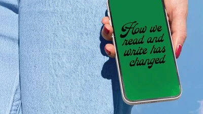 "Hand holding smartphone with green screen displaying 'How we read and write has changed', with denim jeans in background.