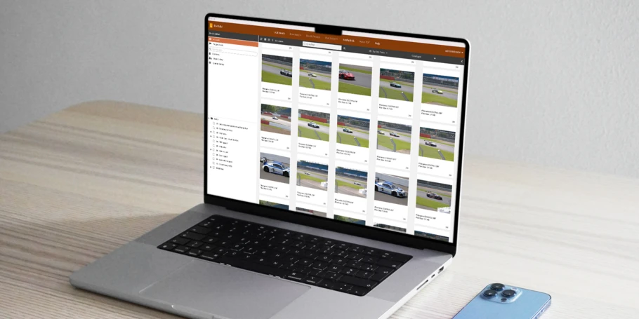 A laptop computer screen displaying the Portrait DAM. The computer sits on a desk with a smartphone face down next to it.